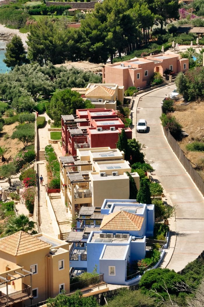 Aerial shot showcasing a vibrant residential area by the coast with lush greenery and winding road.