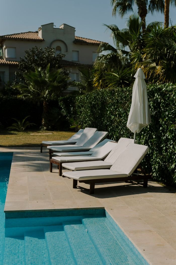 Sunlit poolside with cushioned lounge chairs and lush greenery creates a perfect summer retreat.