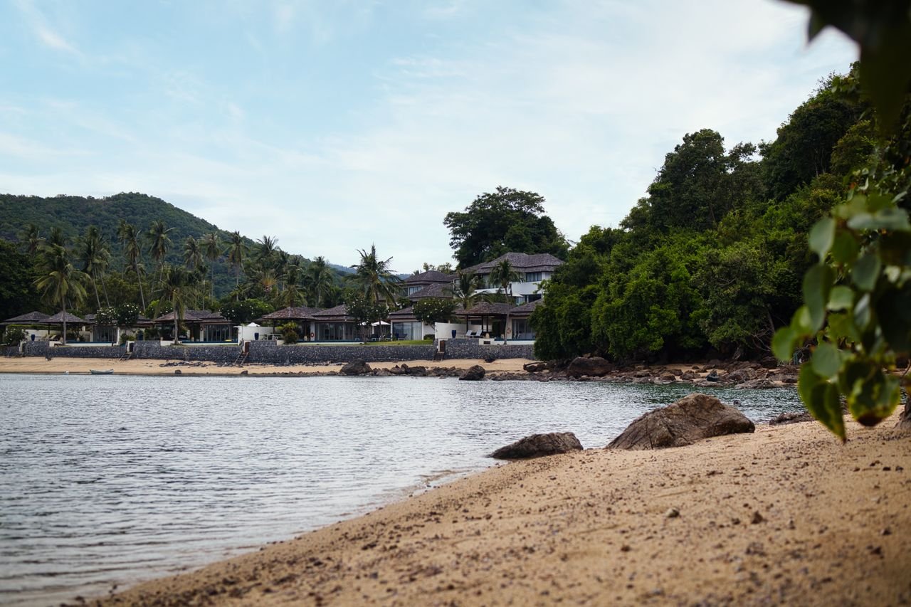 Mastering the First Impression: Your intriguing post title goes here A peaceful tropical beach scene with lush greenery and distant villas under a blue sky.